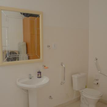 a foto mostra um dos banheiros, com paredes, pia e vaso brancos, um espelho com moldura bege.