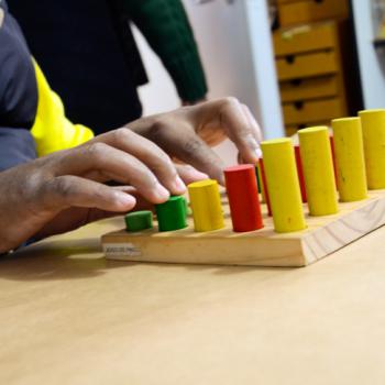 a imagem mostra as mos de um aluno apertando um jogo de pinos coloridos e com tamanhos diferentes.