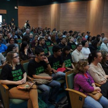 A foto mostra o auditrio lotado, com as pessoas sentadas em cadeiras, algumas j usando a camiseta da campanha.