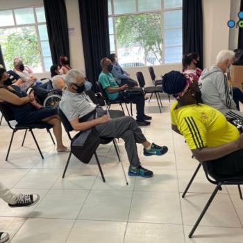 Imagem que mostra, as pessoas olhando para a frente, sentadas de forma esparsa nas cadeiras do auditrio, olhando para a palestrante. No canto superior esquerdo a logo do IPC.